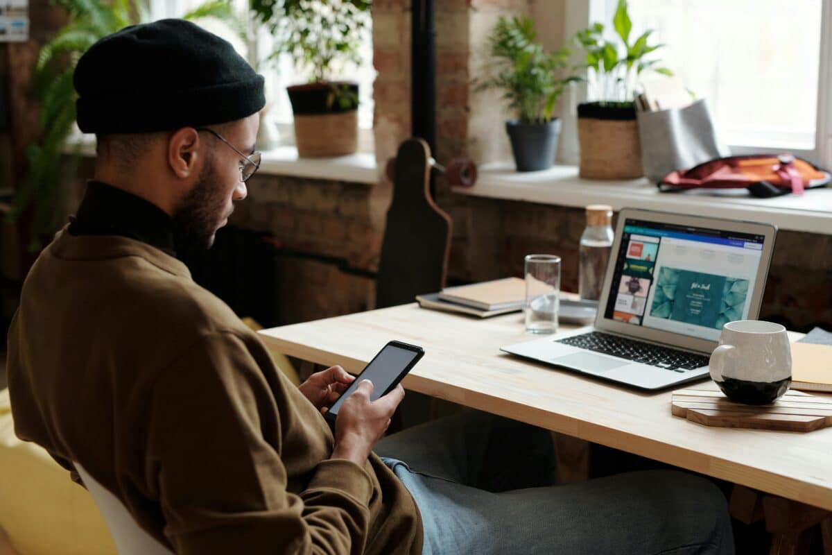 une personne travaillant sur son PC avec un smartphone à la main