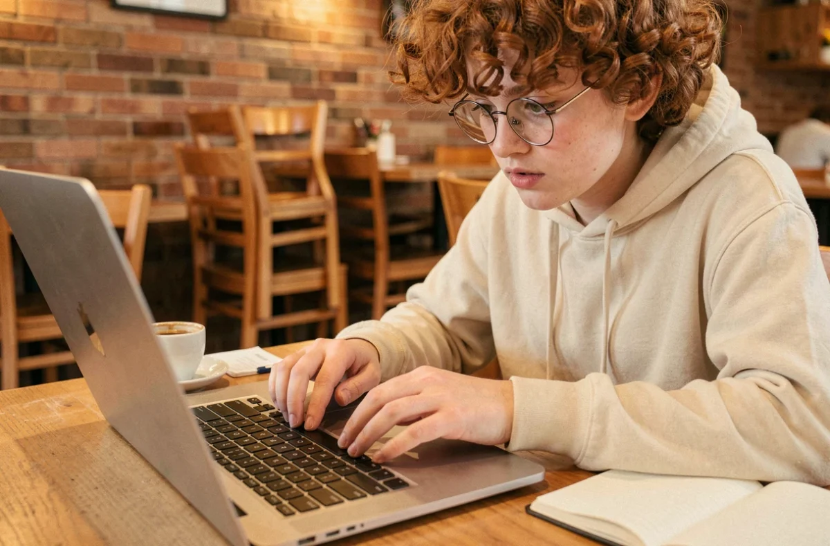 Jeune personne utilisant la touche Shift sur un clavier de laptop dans un café chaleureux